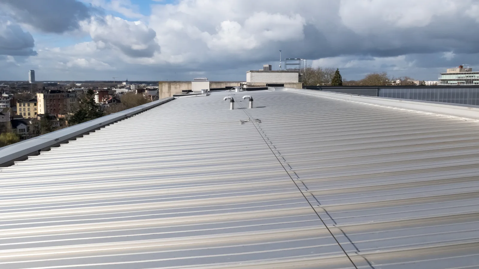 Broad low-slope metal roof with raised seams and small roof penetrations
